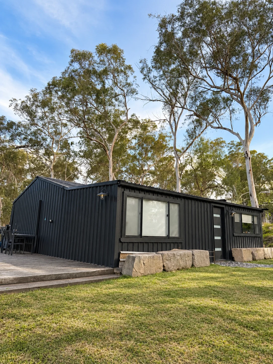 Separate dark-clad house with timber deck, stone garden edging and lawn