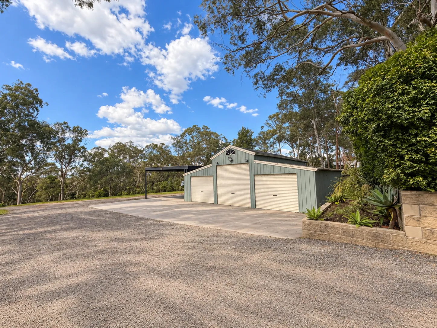 Enclosed shed with roller doors, adjoining covered parking and broad gravel approach at 302